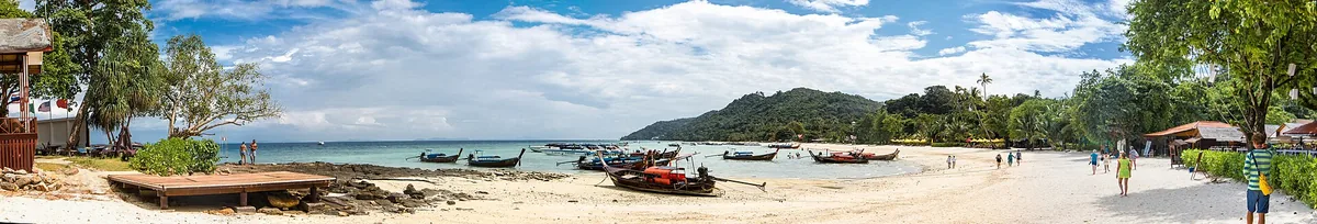 Longtail boats drawn up on the sand at Ao Nang beach beneath a wooded limestone headland.