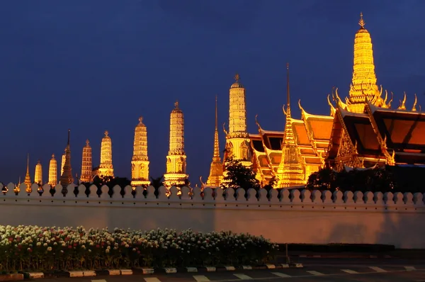 The golden spires of Wat Phra Kaew and the Grand Palace lit against a deep blue evening sky.