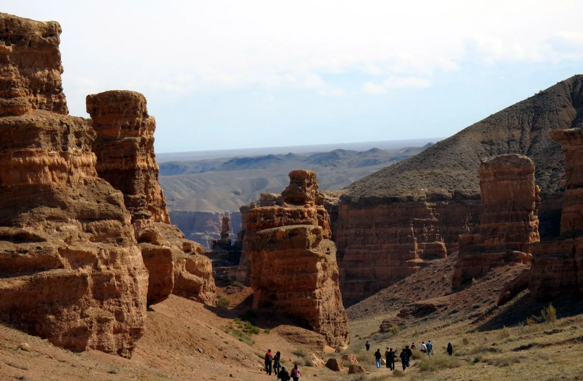 Red sandstone towers in the Valley of Castles at Charyn Canyon, walkers on the floor for scale.