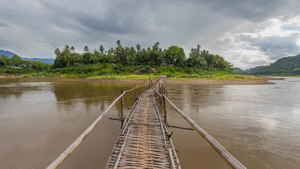A bamboo footbridge across the Mekong to Luang Prabang, hills behind.