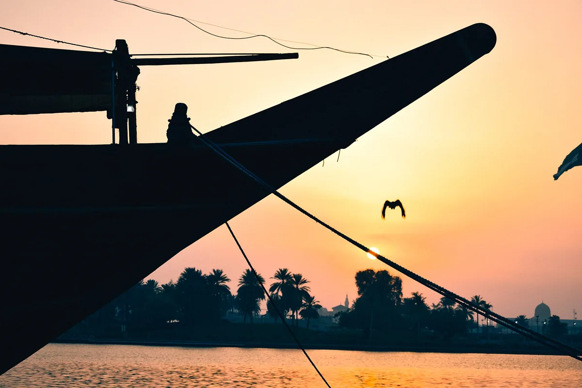 A dhow moored on the Sharjah creek at sunset, palms along the far bank.