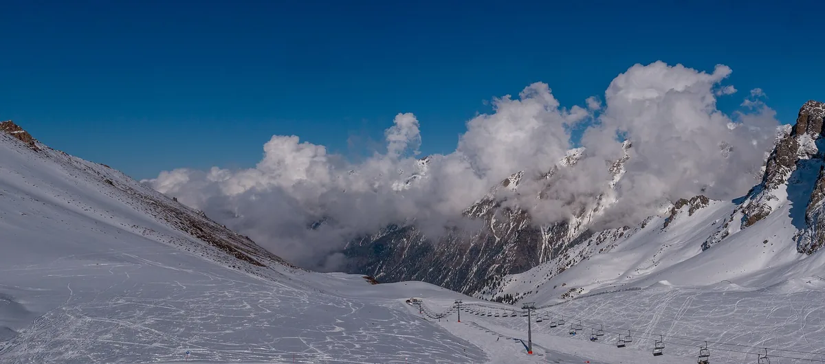Snow-covered slopes and a chairlift line at Shymbulak above Almaty, cloud on the ridge.