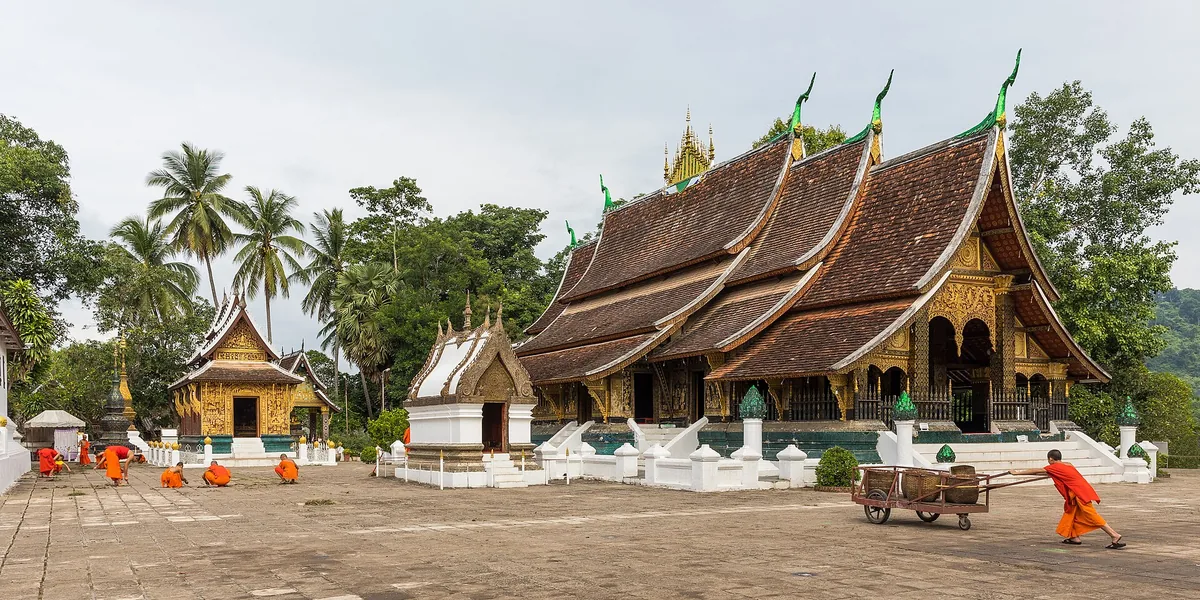 The sweeping roofs of Wat Xieng Thong in Luang Prabang, monks crossing the yard.