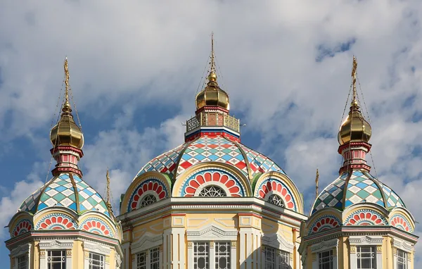 The painted domes of Zenkov Cathedral in Panfilov Park, Almaty, against a blue sky.