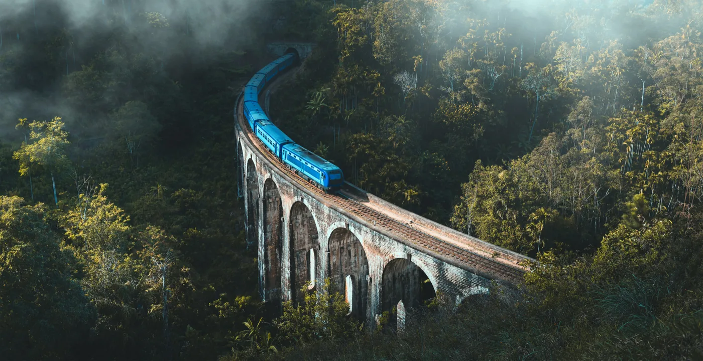 A blue train crossing the Nine Arches Bridge above the forest at Ella, Sri Lanka